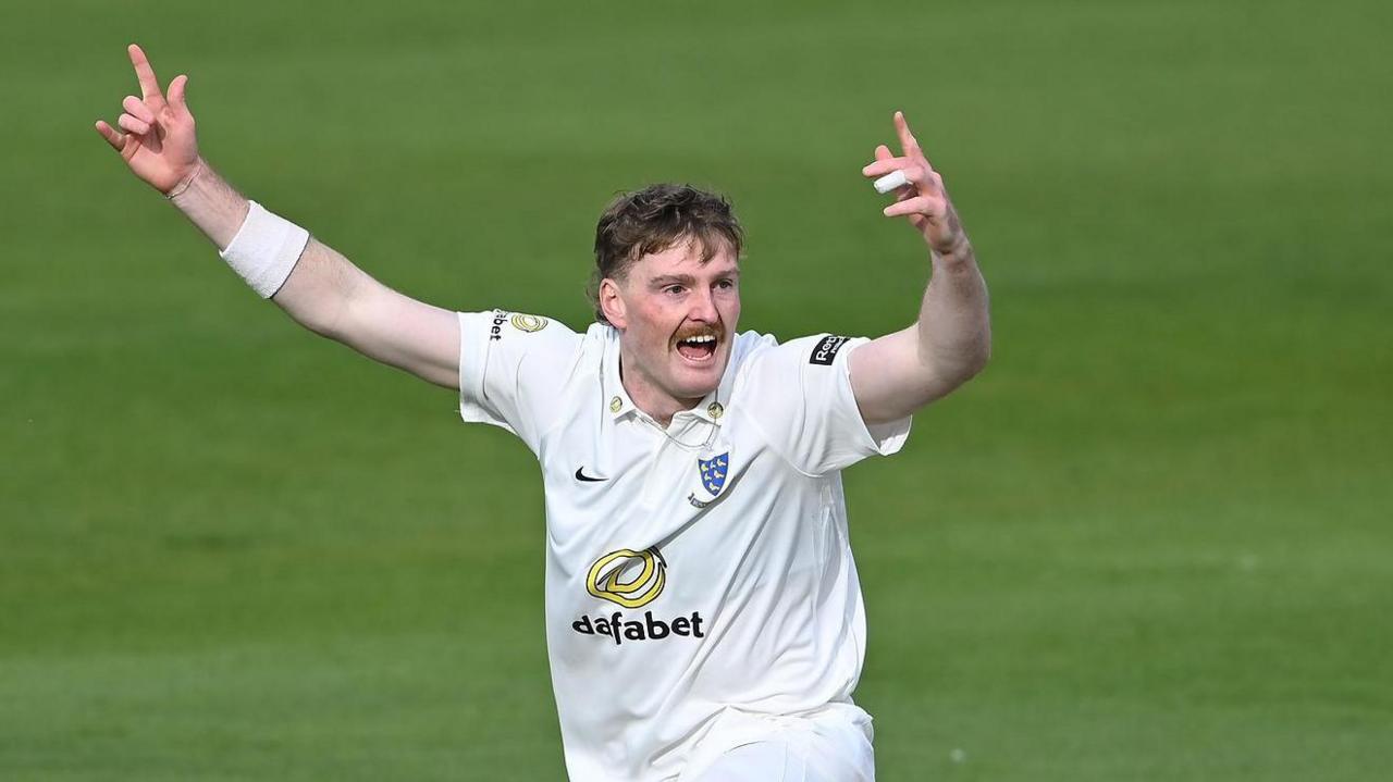 Sussex bowler Sean Hunt celebrates with hands aloft after taking a wicket