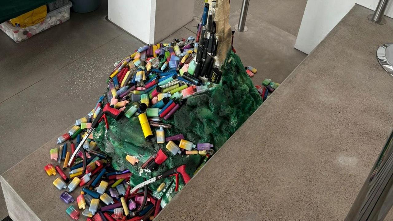 The sculpture consisting of thousands of disposable vapes of many different colours and designs. Green material is also part of the base.