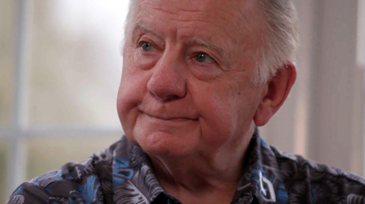 A man with grey hair and a patterned shirt looks away from the camera, with tears in his eyes