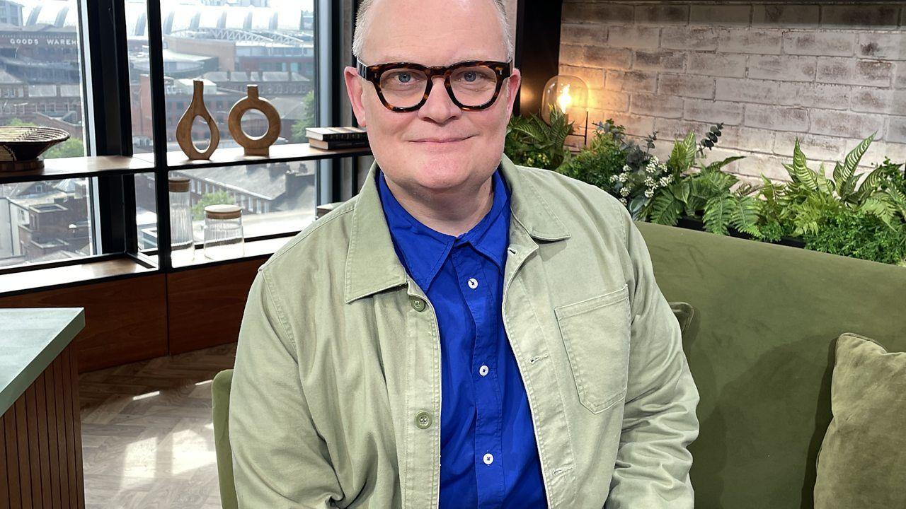 Gary Rycraft is a white male wearing horn-rimmed glasses, a blue shirt and light green jacket. He sits on the Morning Live studio sofa. 