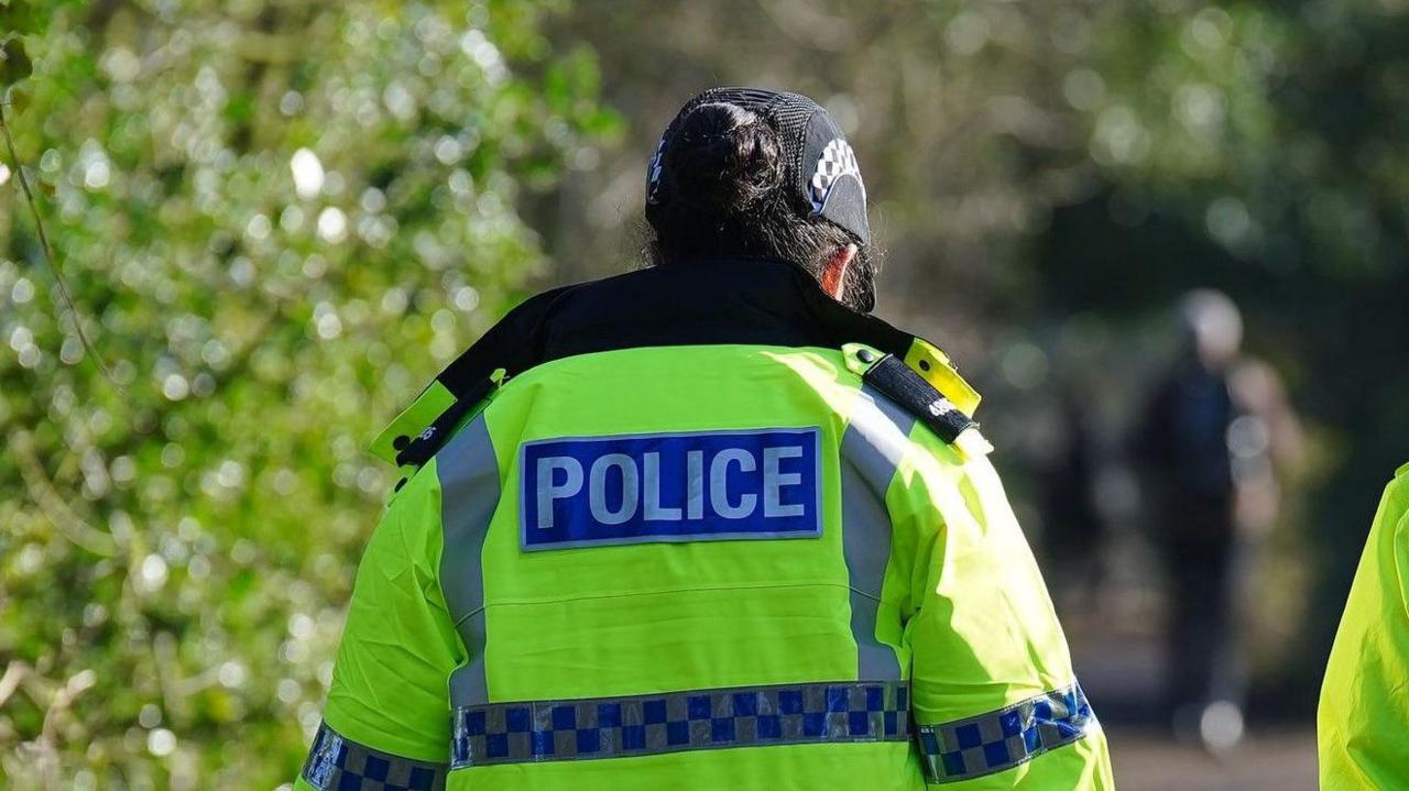 Officer with their back to us wears a fluorescent jacket with police on it