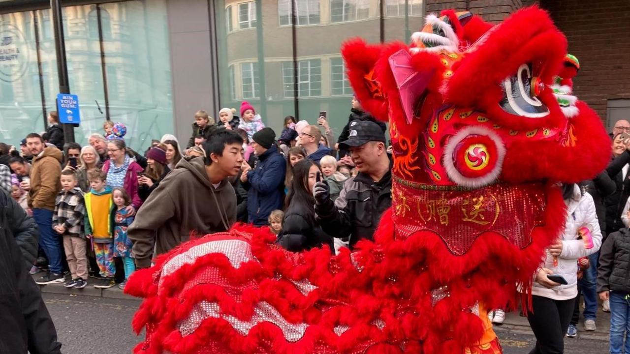 A red horse passes along the street watched by many children as part of a parade to mark the Chinese New Year 