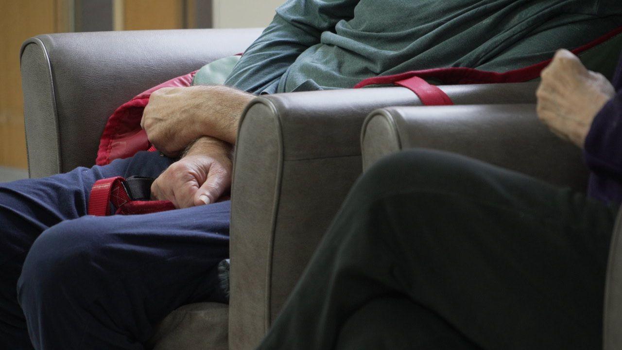 Care home residents sitting in chairs. Their hands, legs and lower torsos are visible.