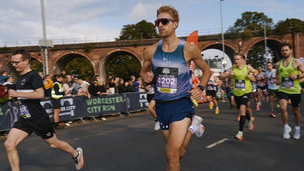 An image from last year shows one man most prominent in the middle, running and wearing sunglasses. Another runner is on the left with at least half a dozen people behind him. Crowds are behind barriers on the left of the photo.