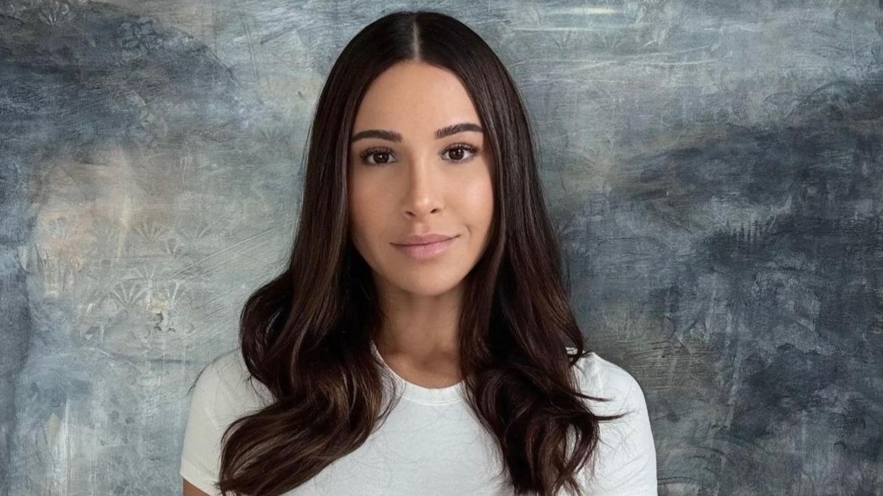 Lauren Pisciotta, has long dark hair and is looking into the camera while wearing a white top