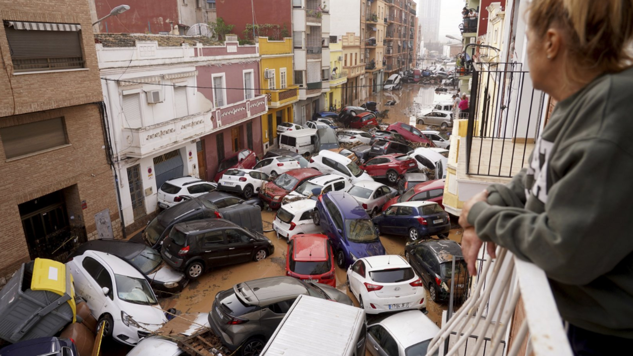 A woman looks out from her balcony at a pile up of scores of cars in a flooded street in Valencia on 30 October