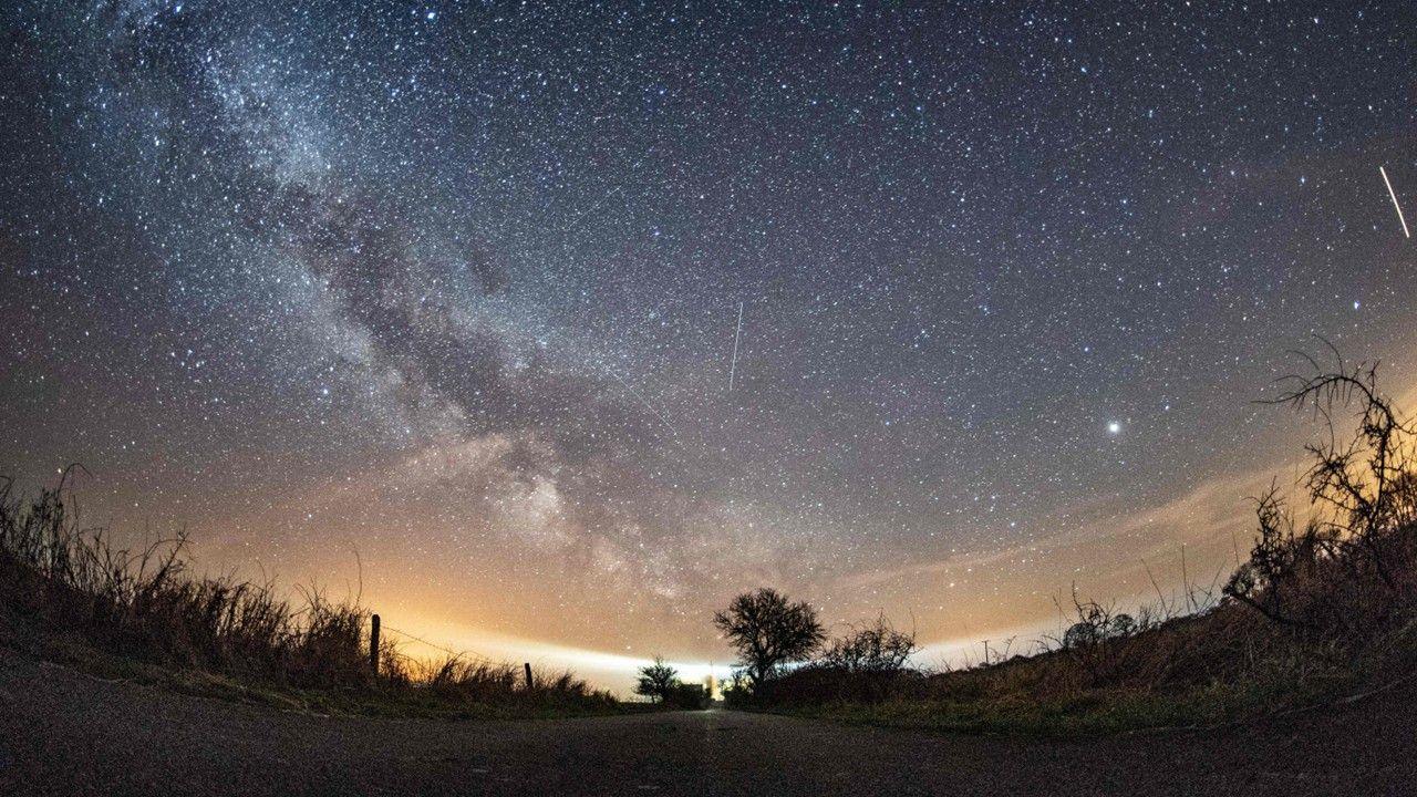 Masses of white stars shine out in the sky with the cloudy streak of the Milky Way from the left to the centre, with occasional white streaks in the sky from Lyrid meteors