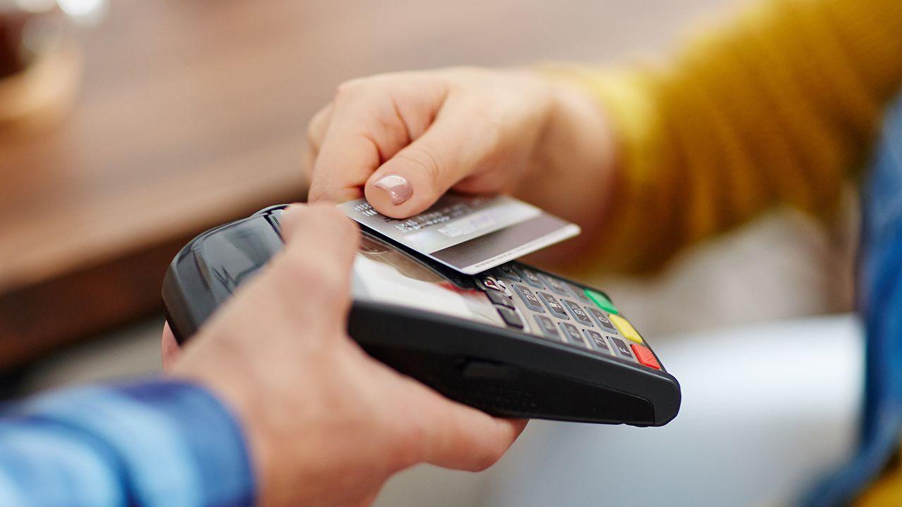 A close up of a person tapping a credit card against a credit card reader to make payment.