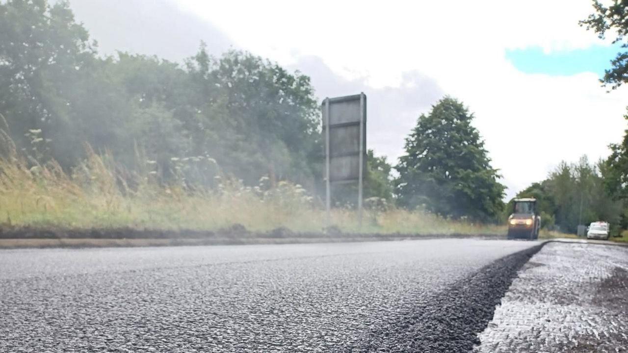 A steamroller is seen in the background with a layer of tarmac being laid on top of the A24