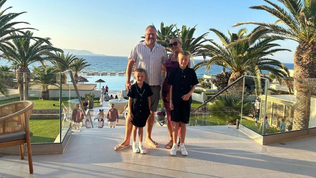 John Gillespie, standing with his family at a resort, the sea is visible behind them