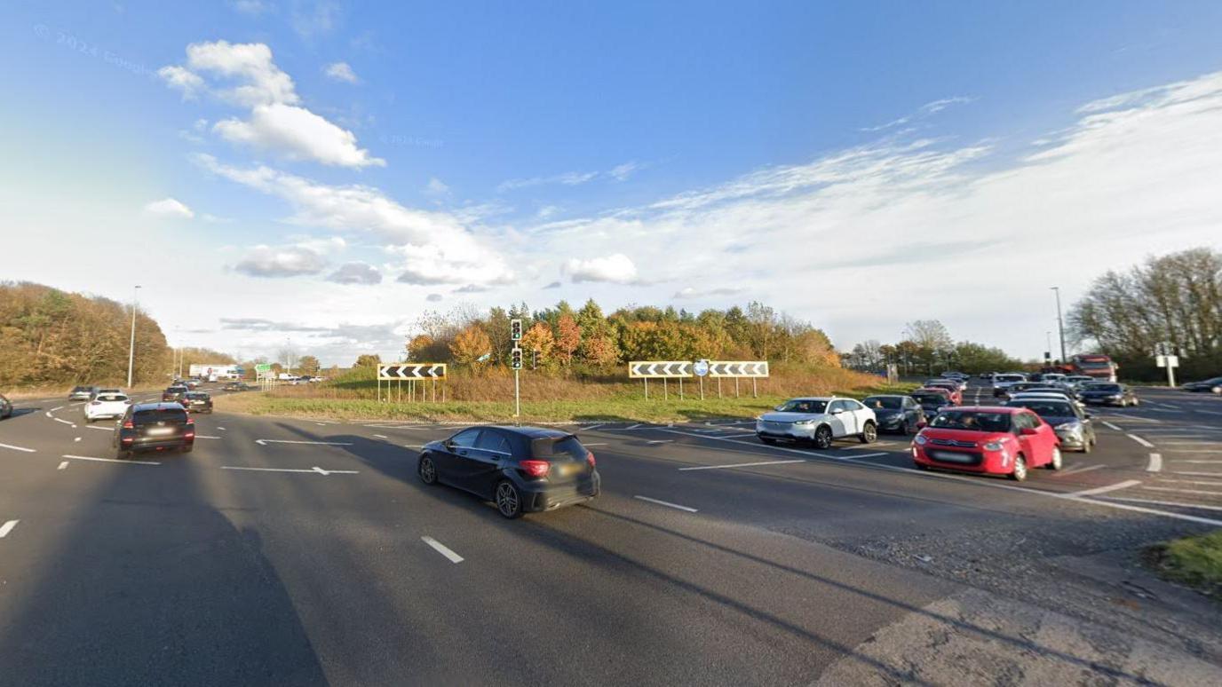 Moor Farm roundabout. It is a busy roundabout with three lanes. The roundabout has grass and trees in its centre.