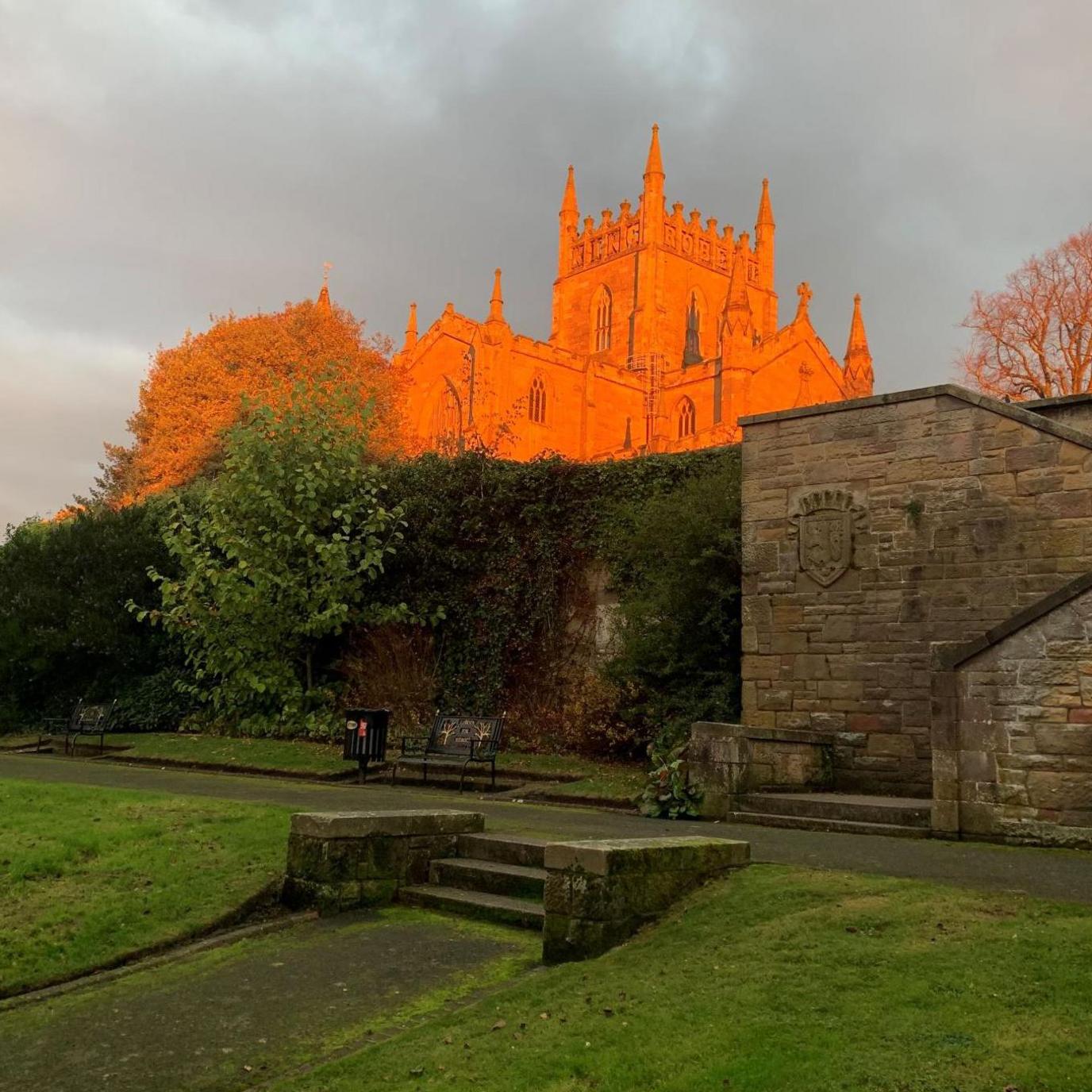 Sunlight gives the abbey and a tree next to it an orange glow. Below the abbey are stone walls and steps.