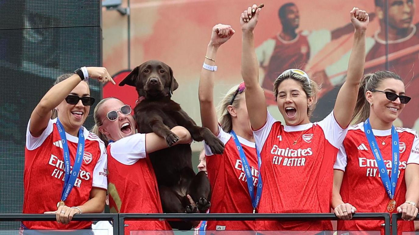 Arsenal players lift up Win the club dog