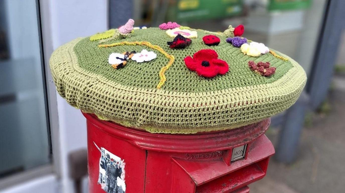 A red post box is seen with a knitted decoration on it with poppies to commemorate VE Day in Bedminster in Bristol