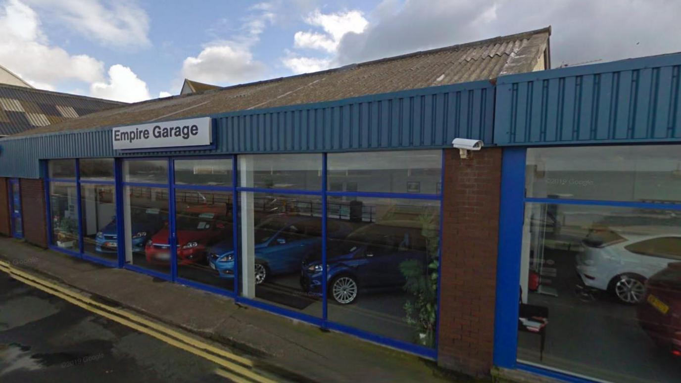 The former empire garage showroom, a blue one-storey building with an empire garage sign and cars inside, the building has large windows.