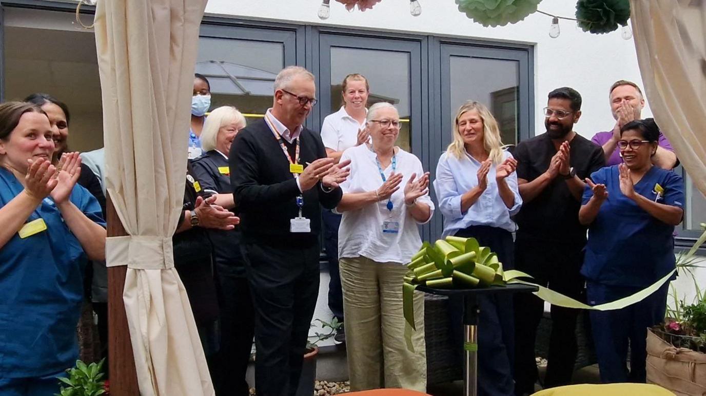 Members of the staff at the ribbon cutting ceremony- clapping their hands- standing under the gazebo 