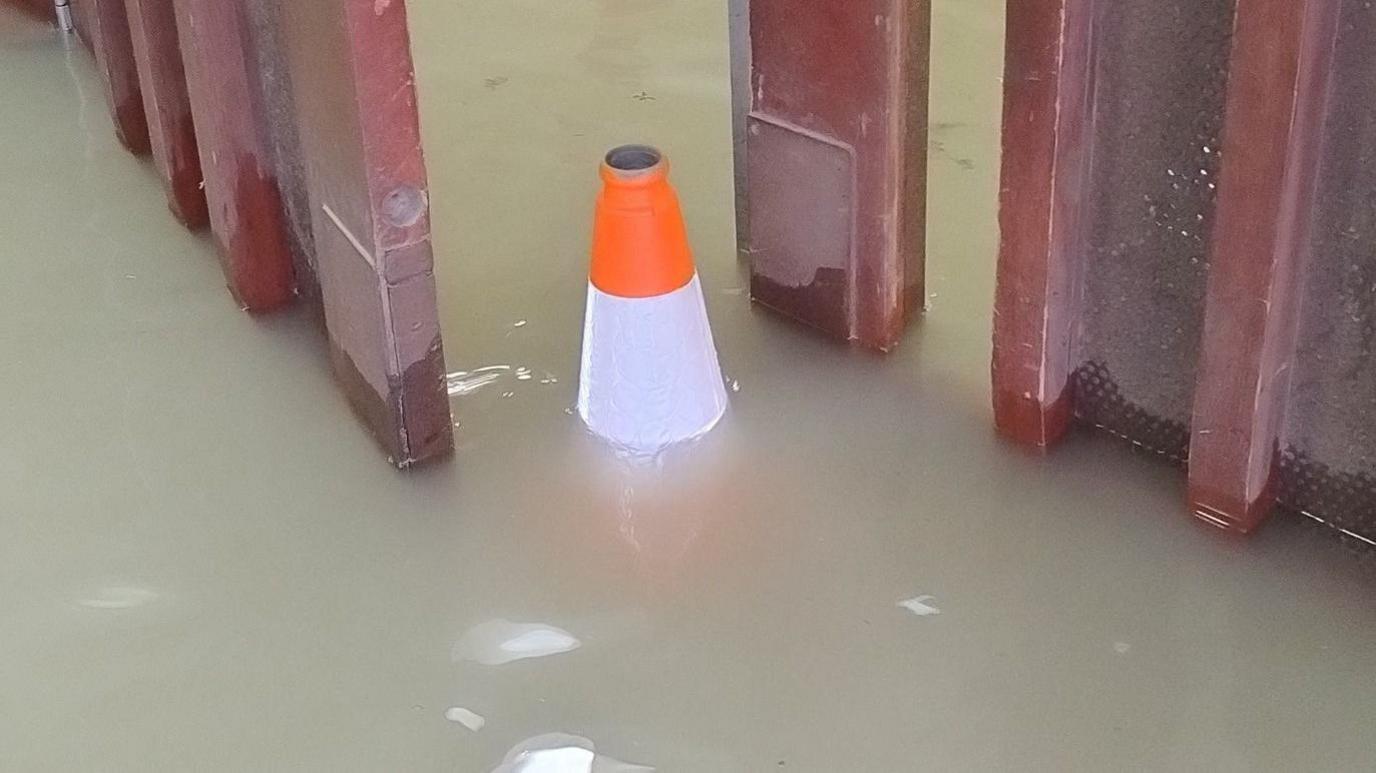 A cone is in the middle of the image in between two red doors. Water is up to nearly the top of the cone and is a light brown colour. 