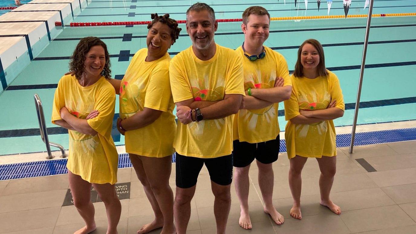 Rosie Eaton, Trish Adudu, Phil Upton, Josh Giltrap and Debbie Woods (left to right) are standing by a pool. They are wearing yellow t-shirts and smiling.
 