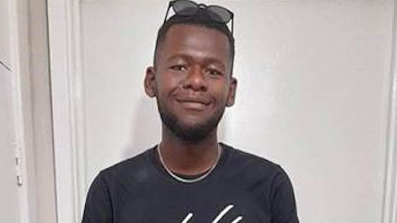 Tyreece Scott is seen smiling and has sunglasses on above his forehead. He is being pictured against a white background.