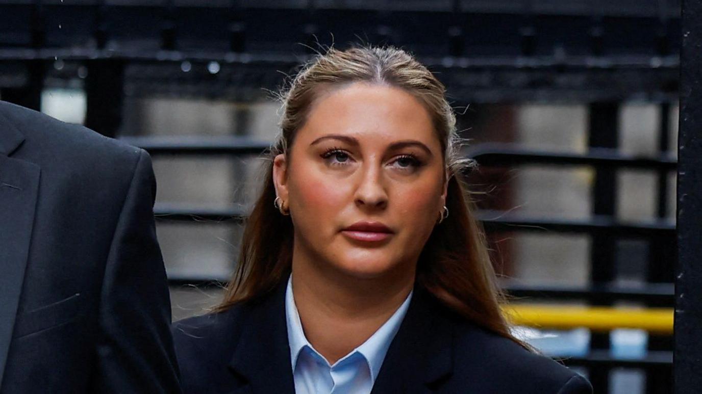 Ms Hand walking through the entrance to the courts, she has long blonde hair and is wearing a blue shirt with a black suit jacket.