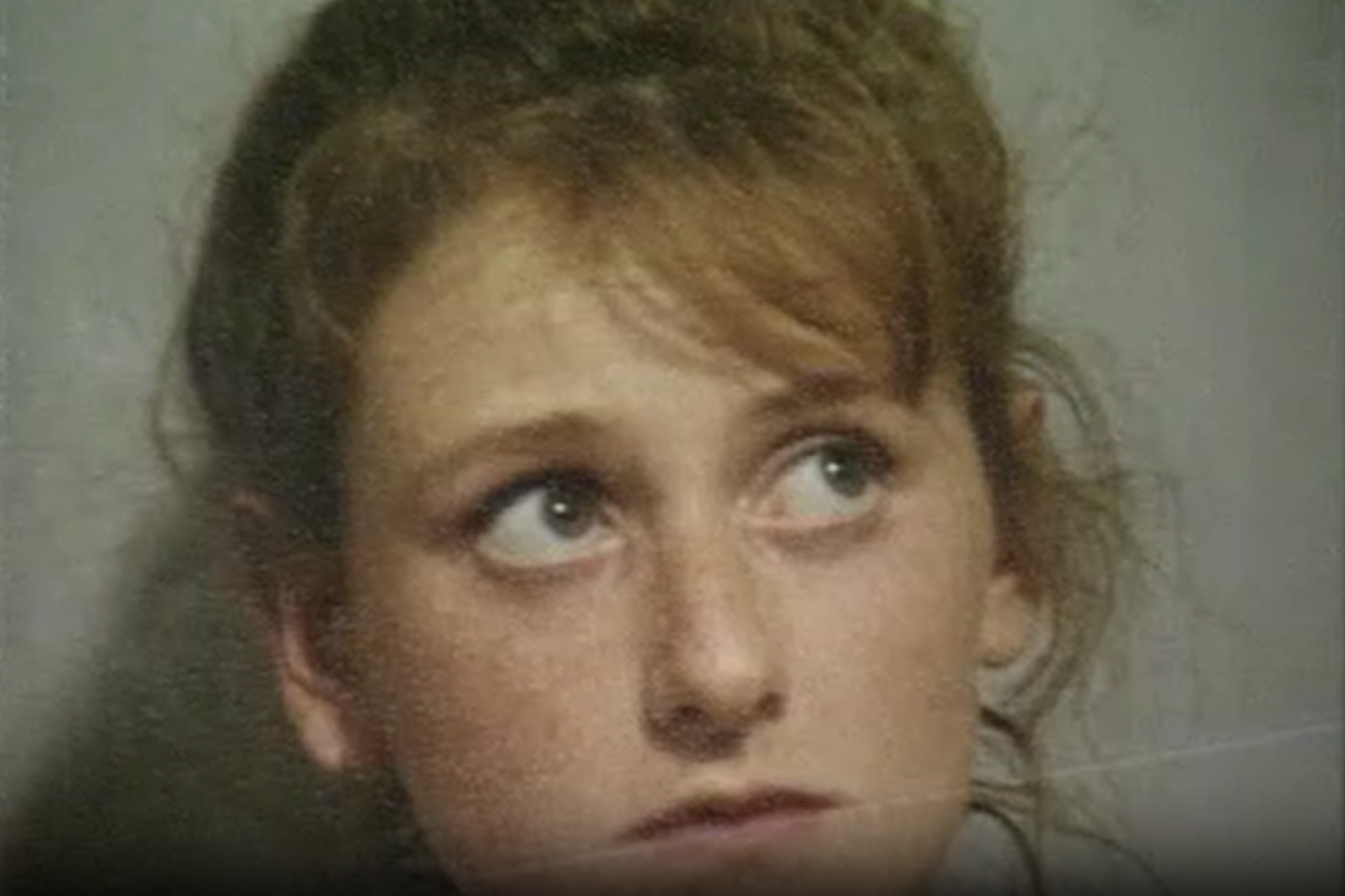 A police mugshot of a young woman with light brown hair glancing up to her left.