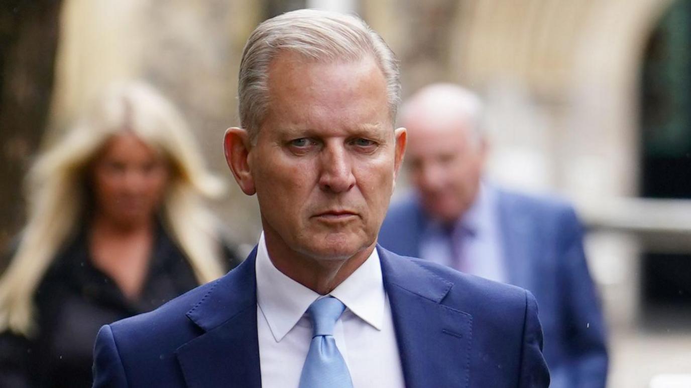 Jeremy Kyle has a grim expression as he leaves the coroner's court in Winchester. He has light, grey hair and wears a blue suit jacket, white shirt and a light blue tie.