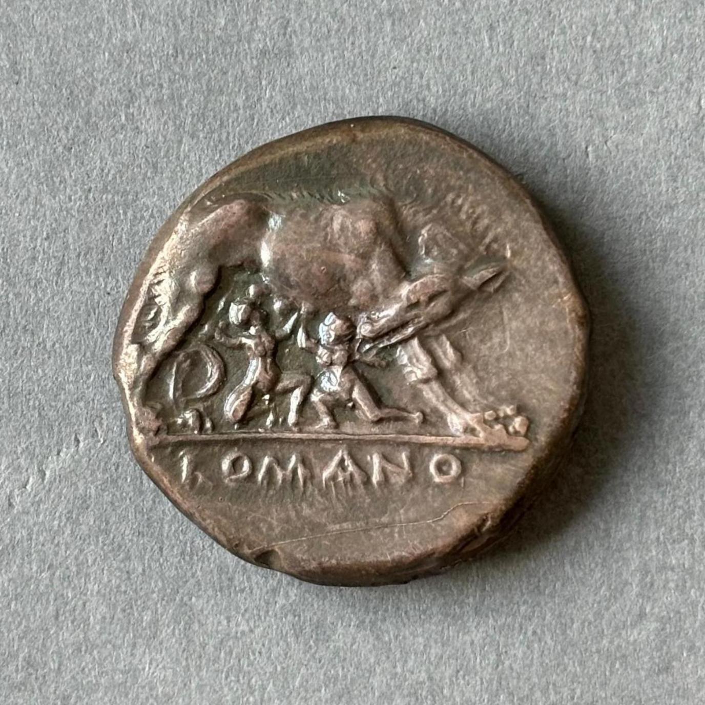 A dark bronze coloured Roman coin depicting the legend of Romulus and Remus, founders of Rome who were raised by a she-wolf. 