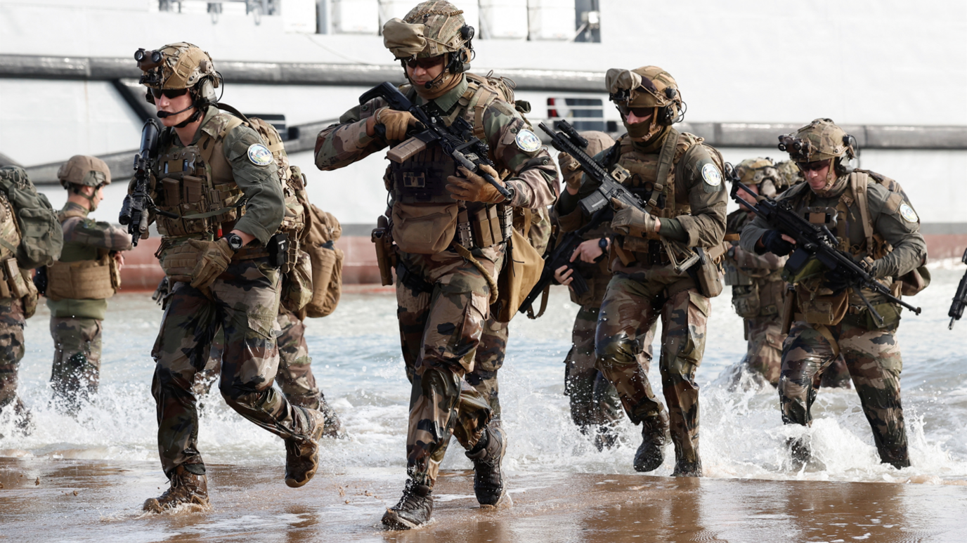 Men in military dress carrying guns on a beach