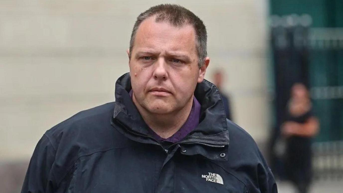 Neil Beckett wearing a black North Face coat with a purple top as he leaves court.