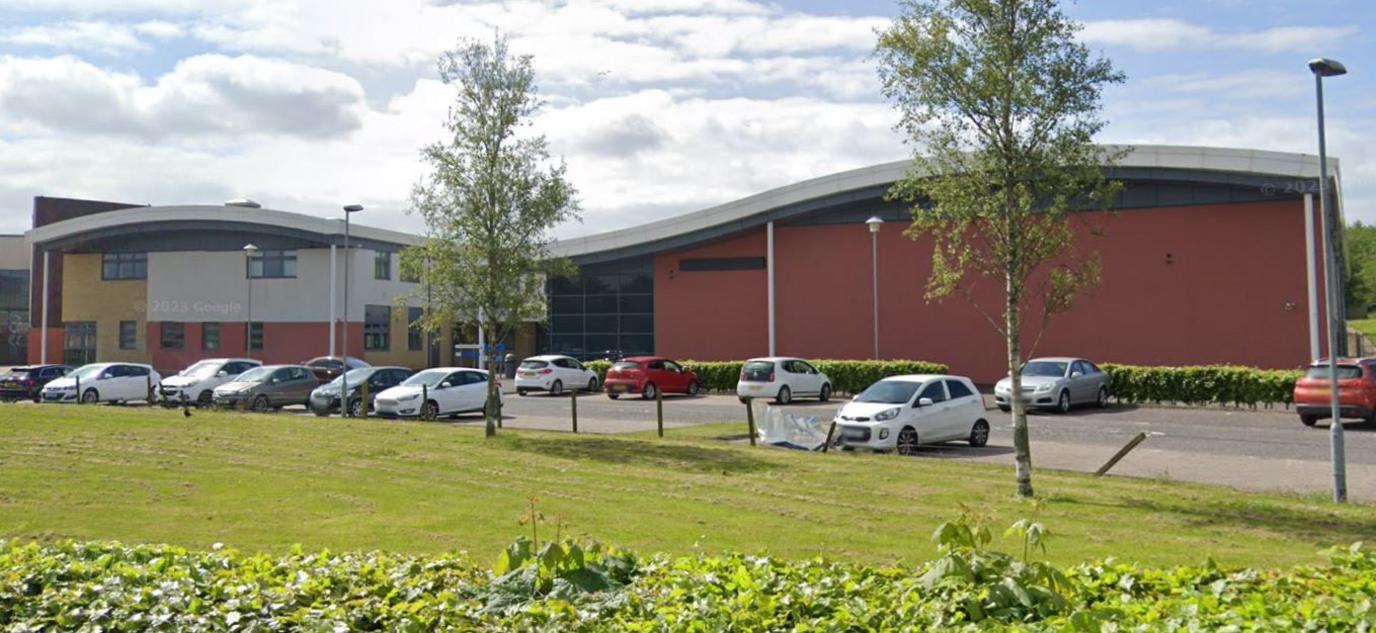 A red and white school building with a curved roof. Cars are parked outside.