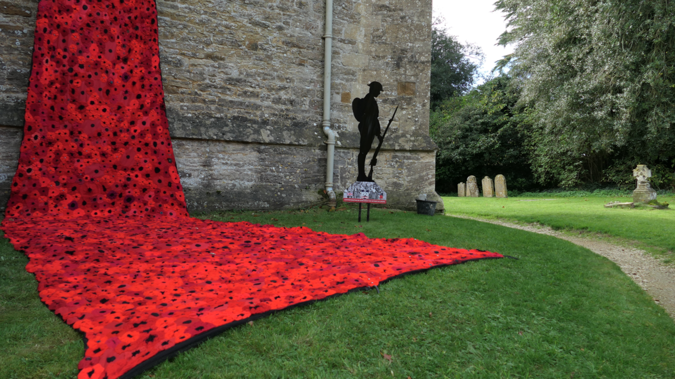 Part of the poppy cascade by the Steeple Aston church. There is a soldier silhouette cut out and some graves are nearby.