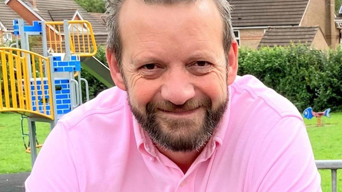 Gavin Heathcote in a pink t shirt in a playground.