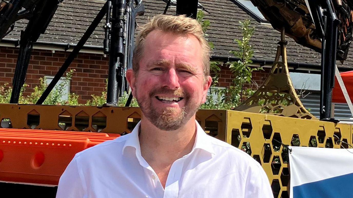 Rugby MP John Slinger looks at the camera wearing a white open-collar shirt.