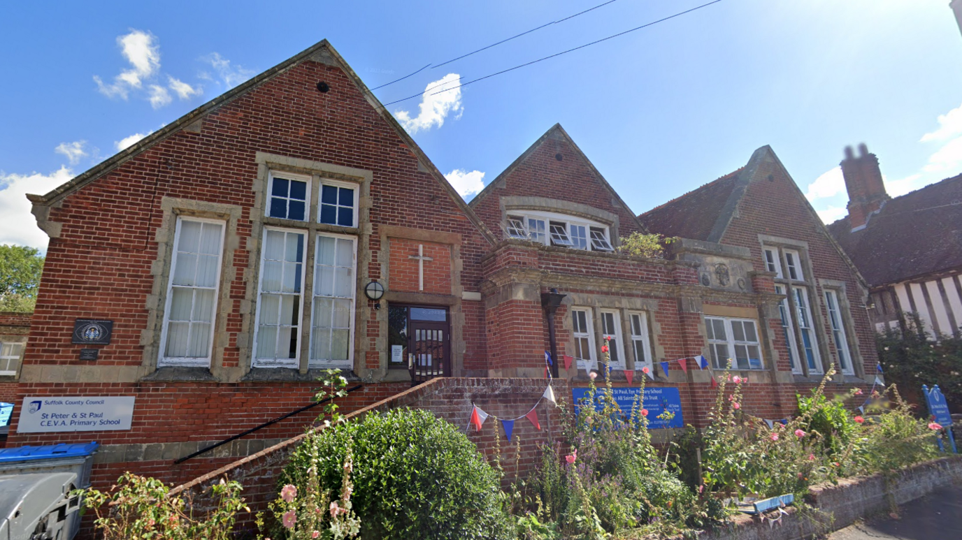 A general view of St Peter & St Paul Primary School. It is a red brick building with large windows. Blue, white and red bunting hangs on the front of the building.