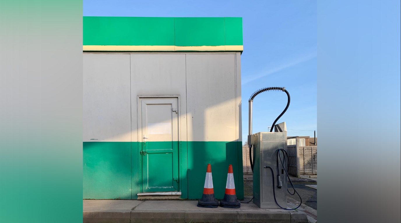 A green and grey striped building has two cones in front of it.