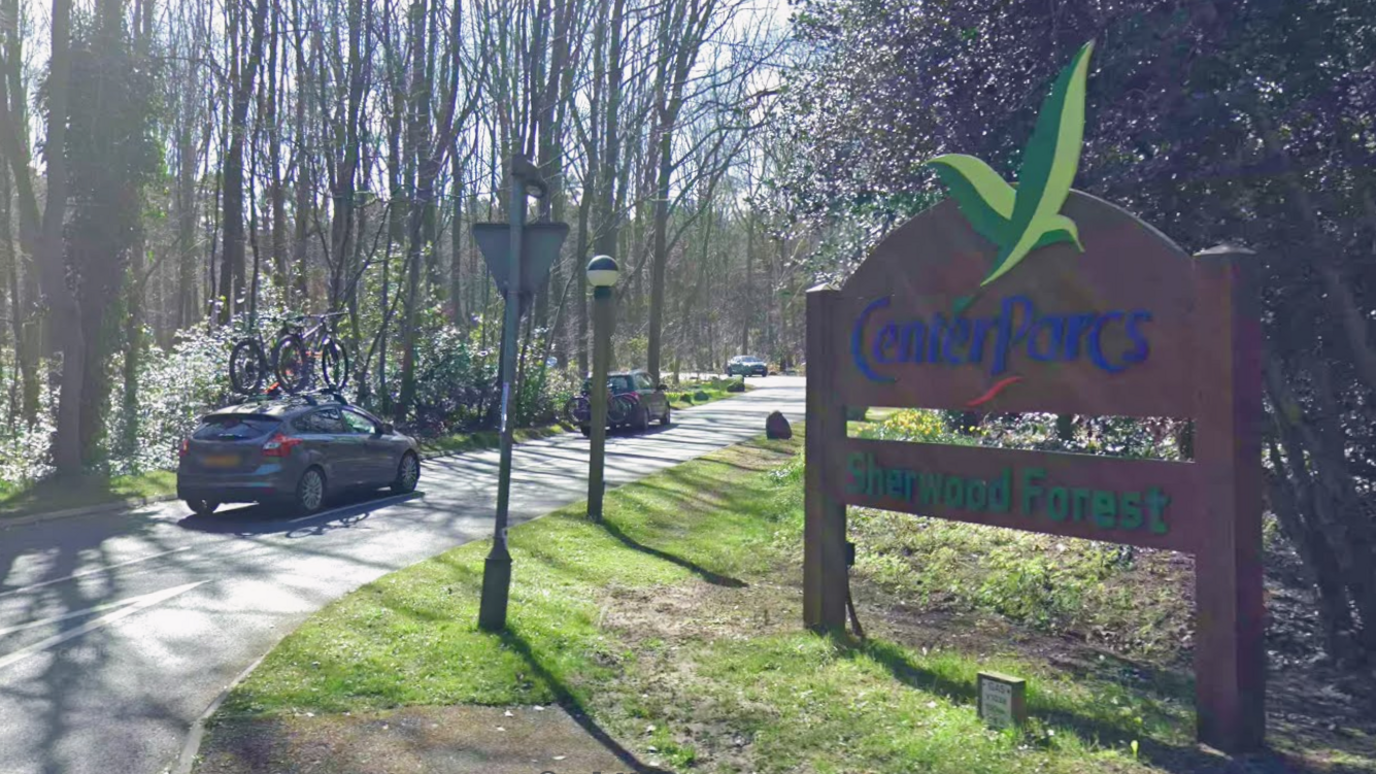 The entrance sign at Center Parcs in Nottinghamshire with cars driving into the site