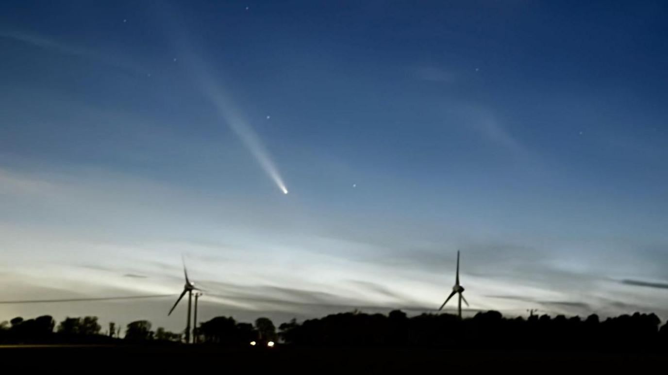 Comet A3 above two wind turbines and trees.