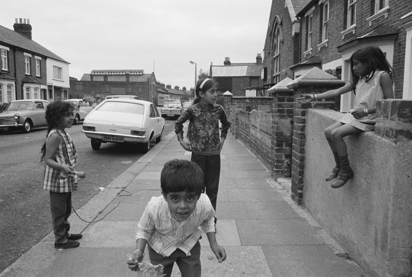 Black and white photograph of four children hanging around on a residential street.