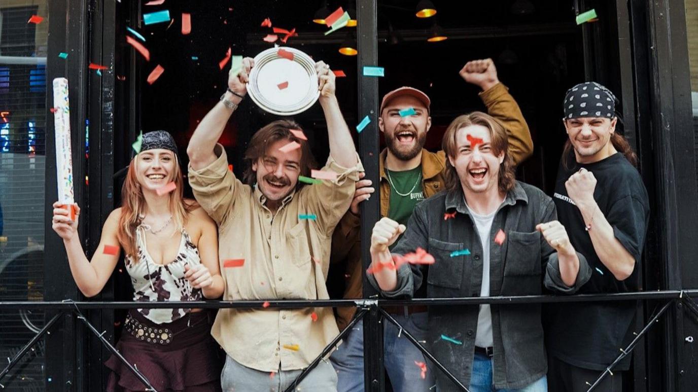 Five staff from Bristol cocktail bar The Juke Box cheer and clench their fists after winning the top prize at Bristol Cocktail Weekend 2025. One of them is holding up a small silver plate.