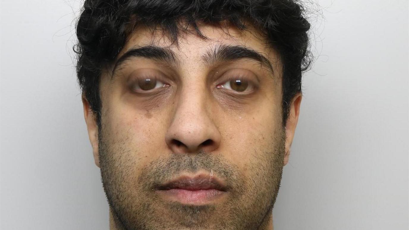 A mugshot of Wiqas Mahmud. He has black hair and facial stubble.