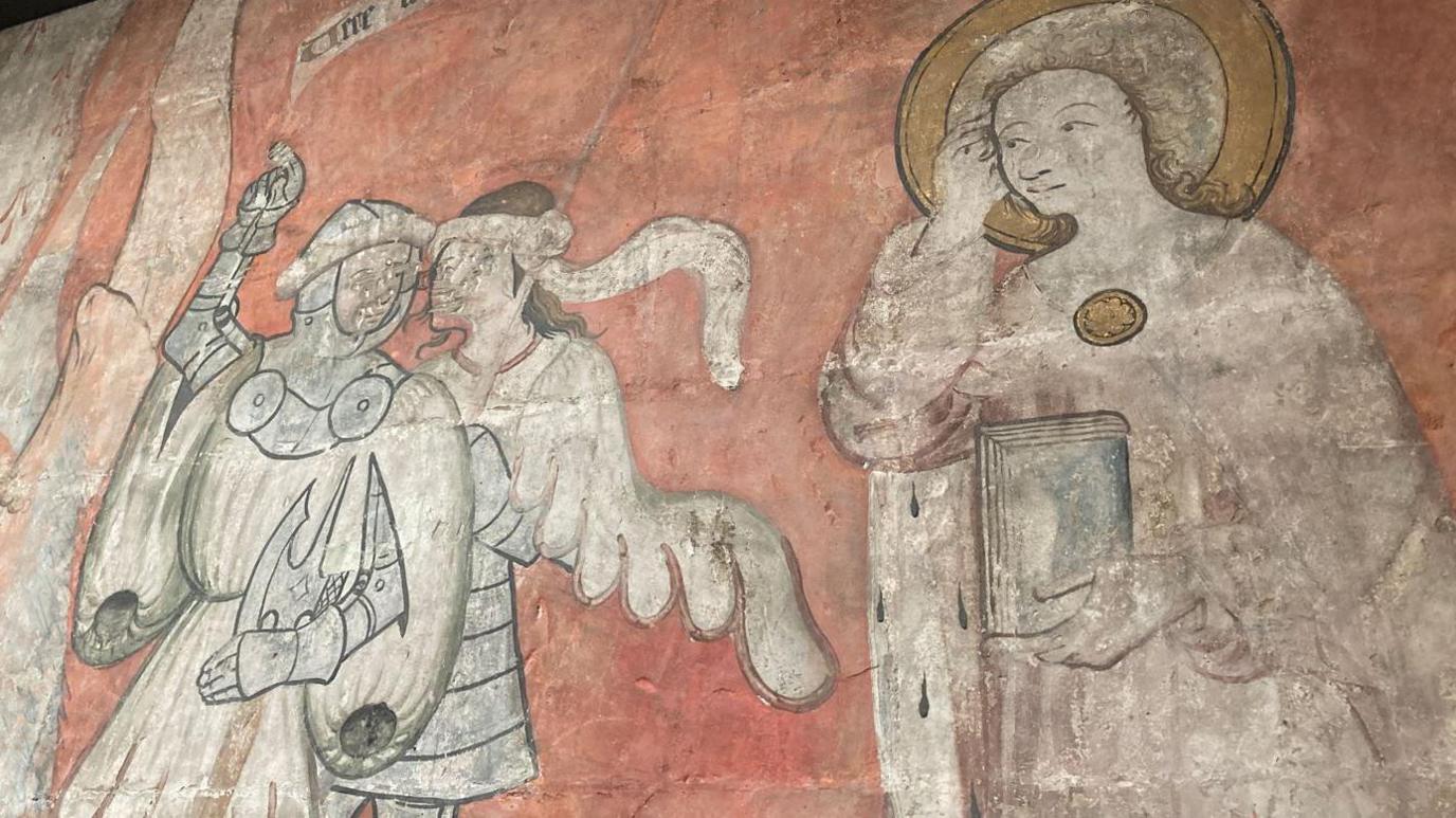 A medieval wall painting showing a saintly figure with a halo facing a man who appears to be a knight and another figure