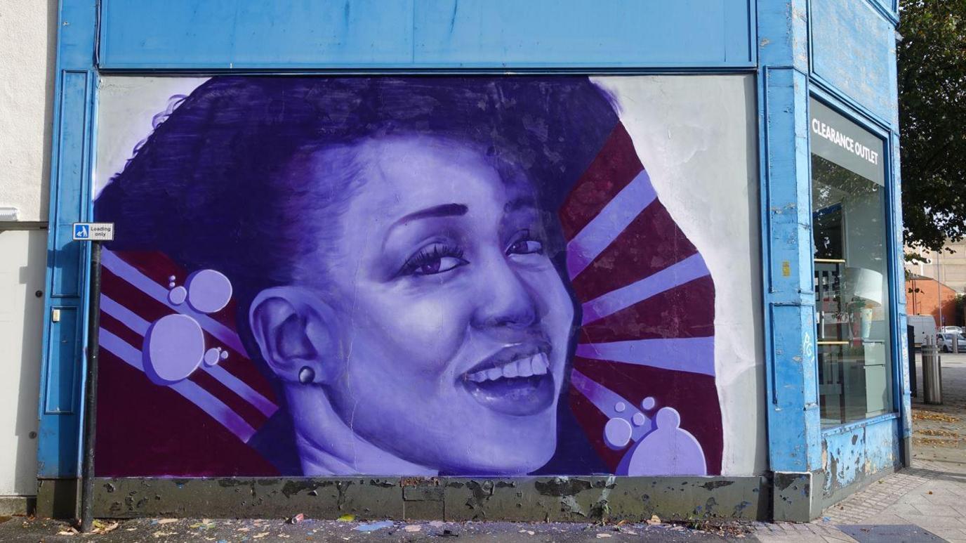 A mural of singer Beverley Knight on the side of a shop. It is painted in purple and shows the singer smiling.