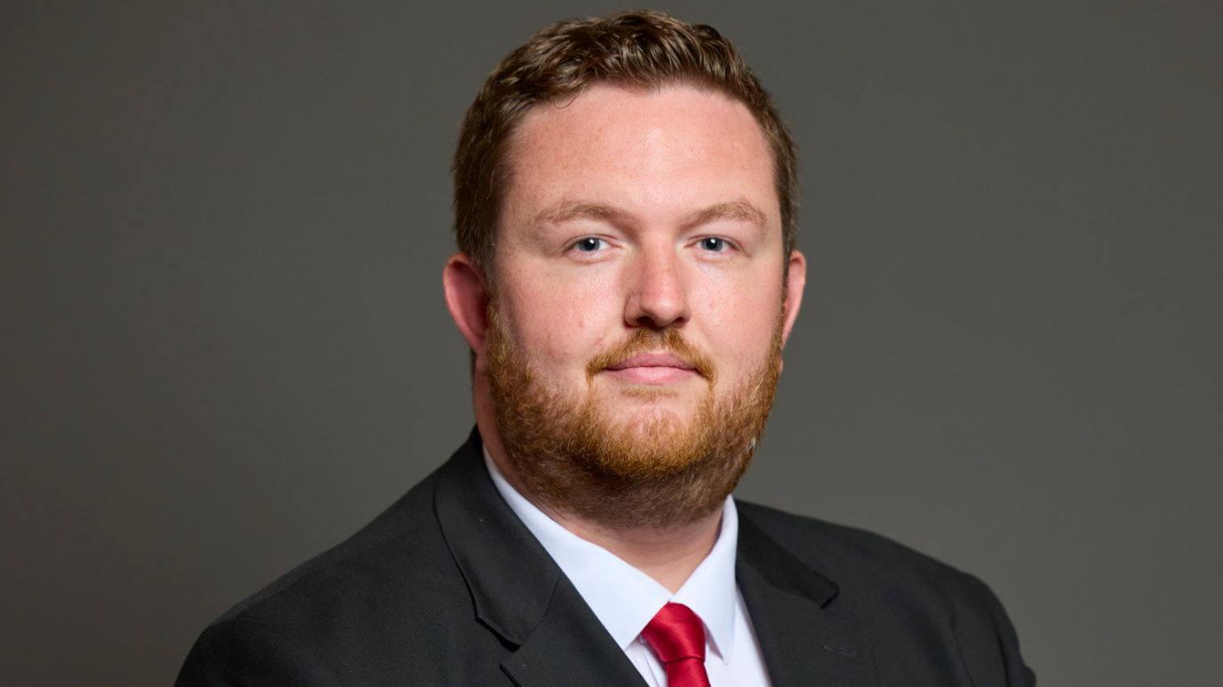 In his official photograph for the House of Commons, Alex McIntyre is looking at the camera and wearing dark smart suit, white shirt and red tie.