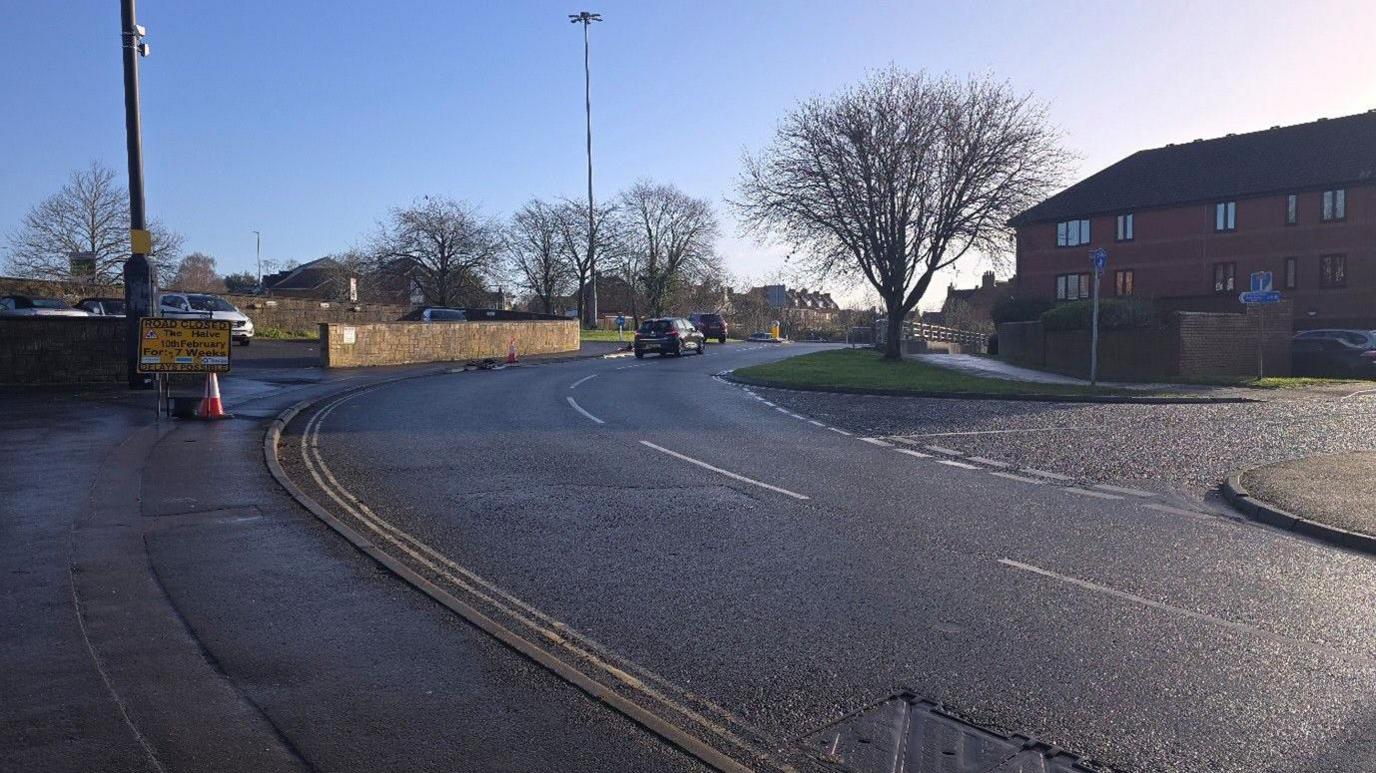 A road with two cars driving along it taken on a sunny winter day.