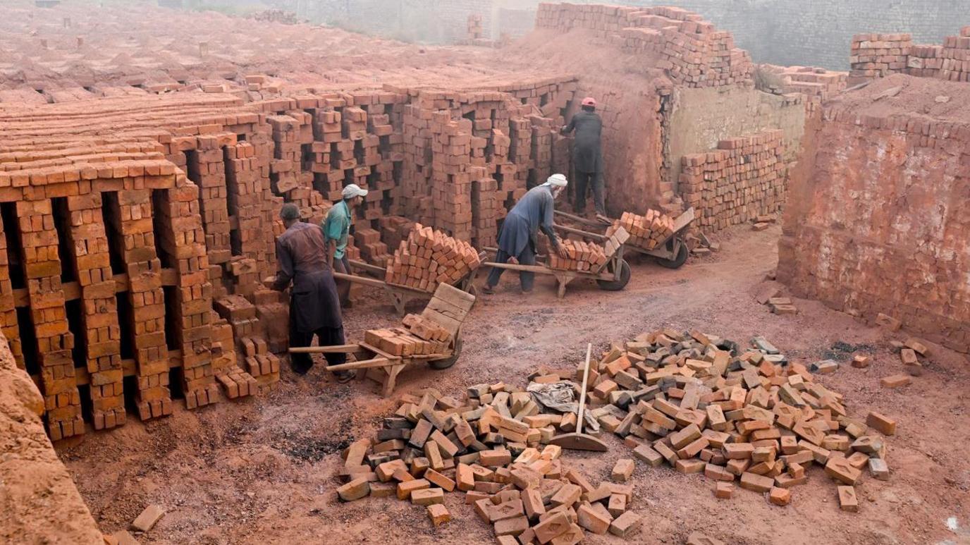 Labourers work at a brick kiln engulfed in smog