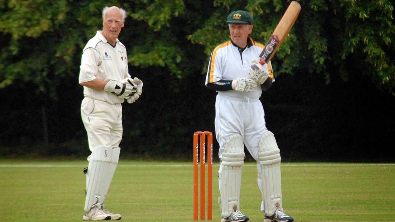 Wicketkeeper Gerald Cooke wearing cricket whites behind the stumps, close to a batsman wearing an Australia kit.