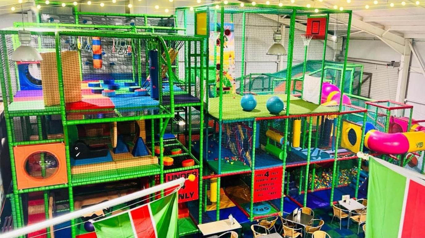 Three story soft play equipment. The frame is green with lots of different coloured apparatus inside.