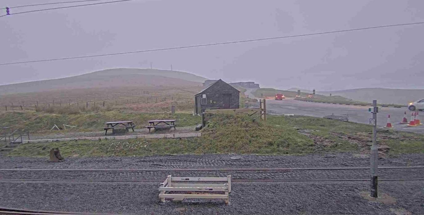 The mountain covered in fog, with a wooden bungalow and picnic benches out.