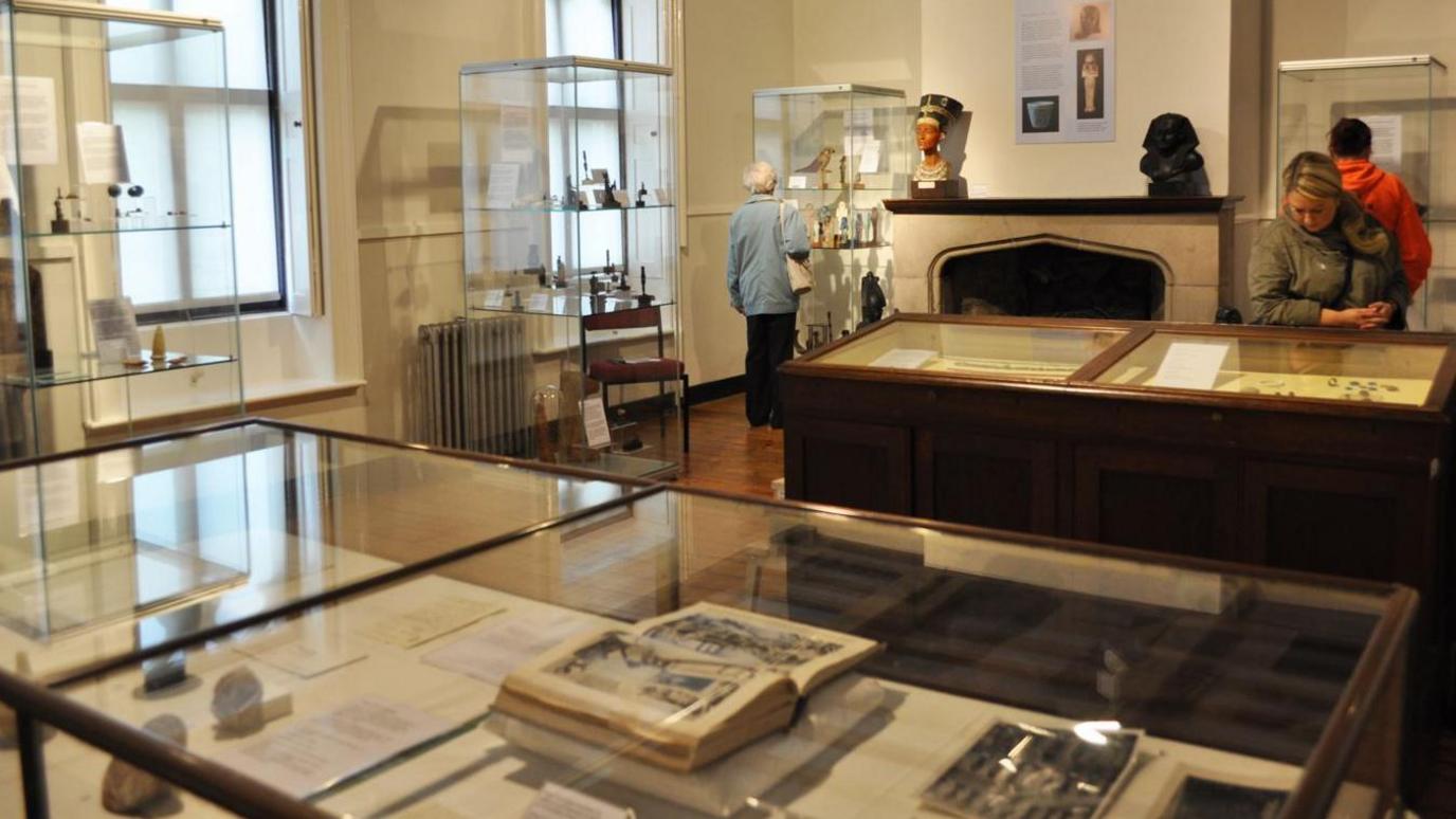 People browse a room full of artefacts in glass display cases.   