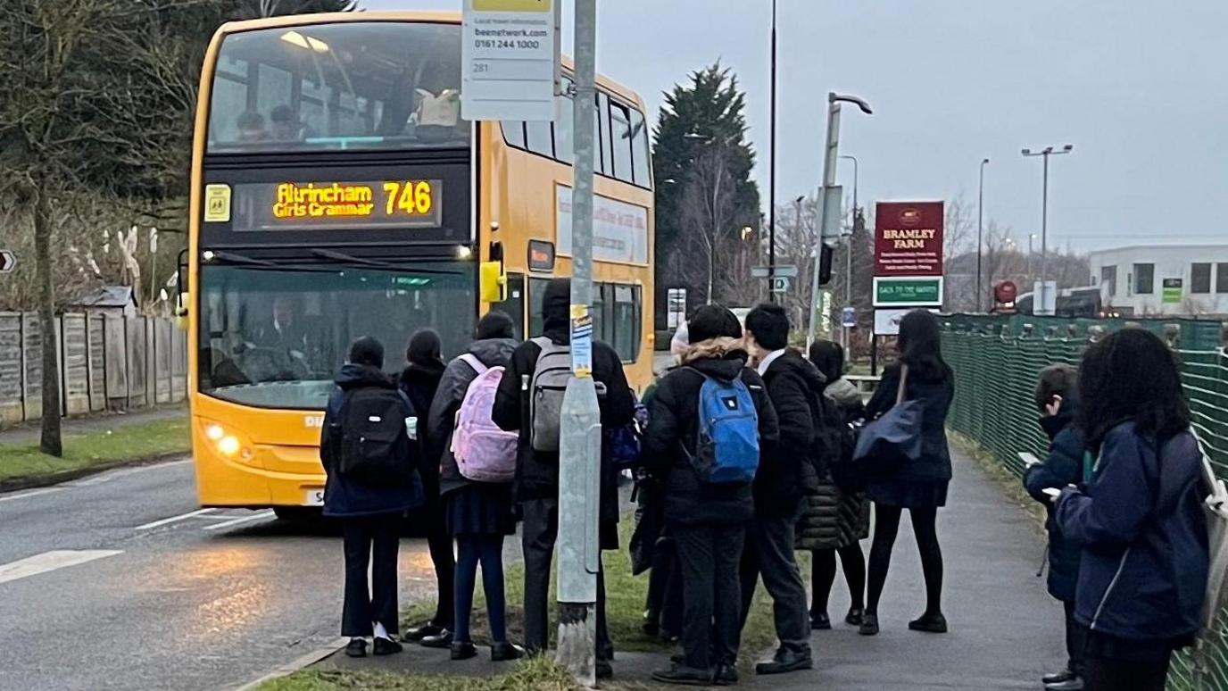 School children waiting for their yellow coloured school bus at a stop.